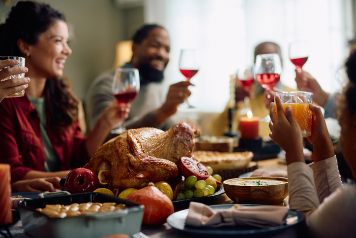 Roast turkey with family toasting during Thanksgiving meal Tat dining table.